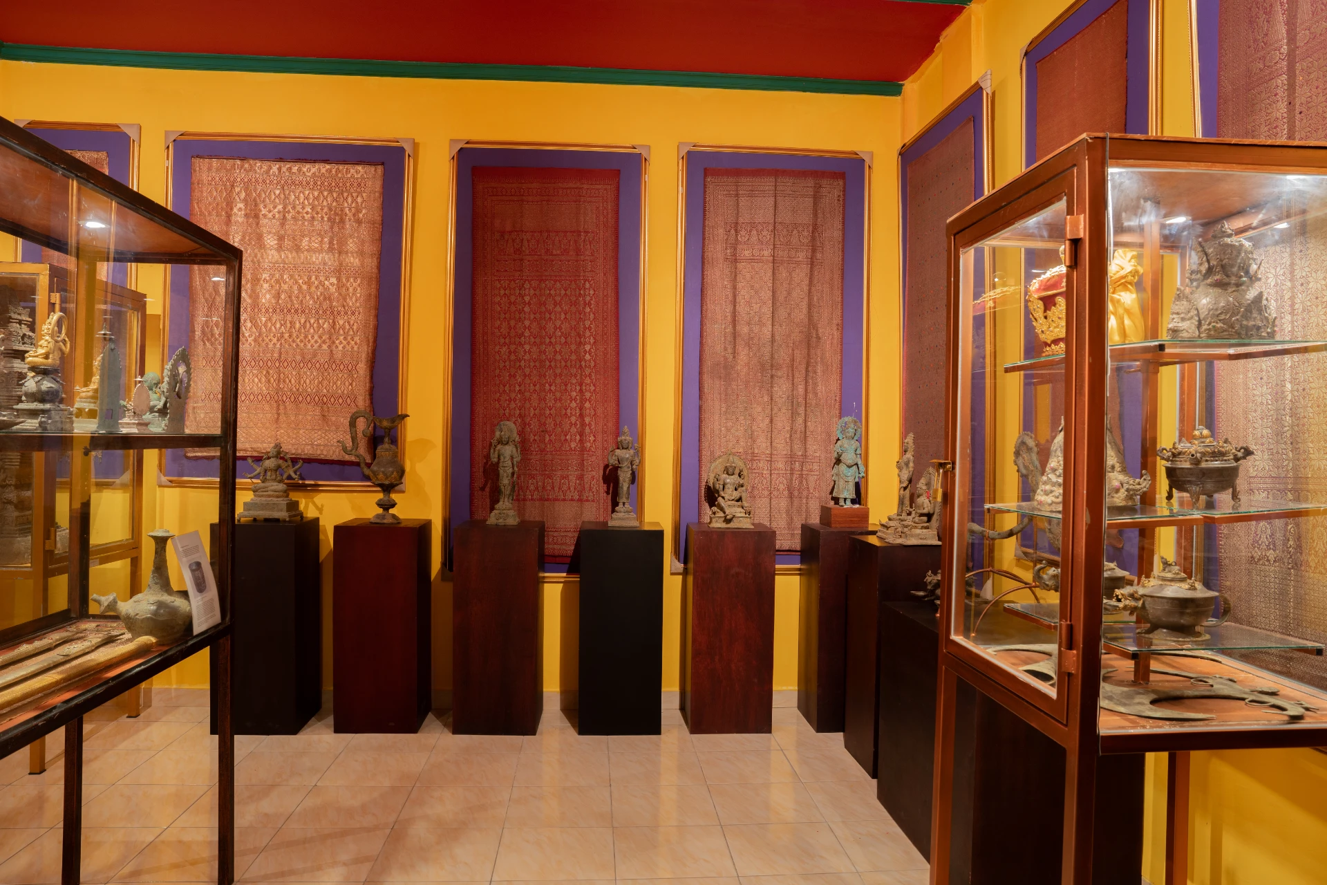 Curated glass display cases featuring historical artifacts and stone sculptures, Museum Peter Bloch Collection gallery.