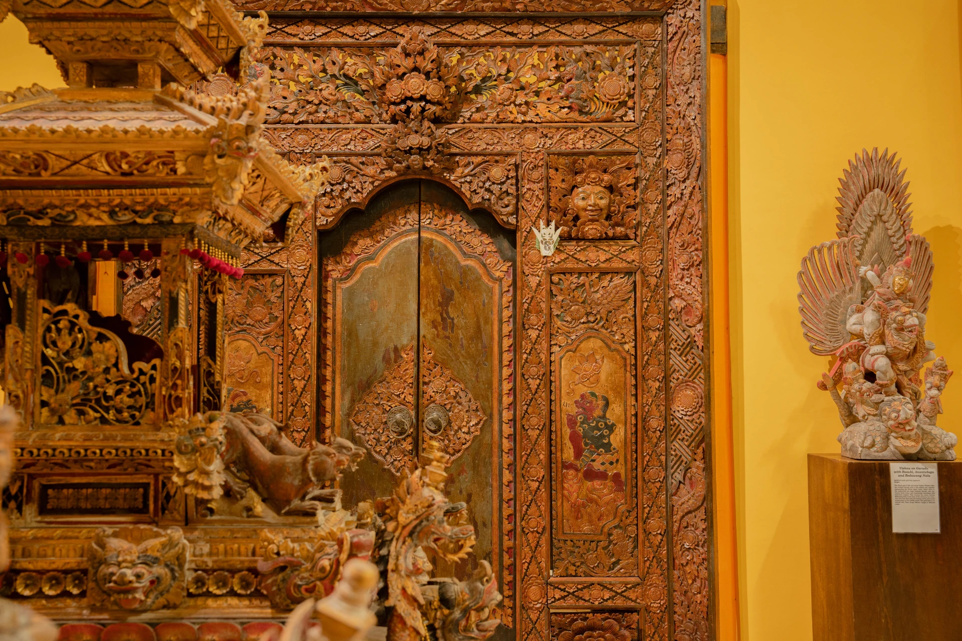 Traditional Balinese carved wooden doorway with intricate ornaments and ceremonial textiles, Annemarie Kipar Room.