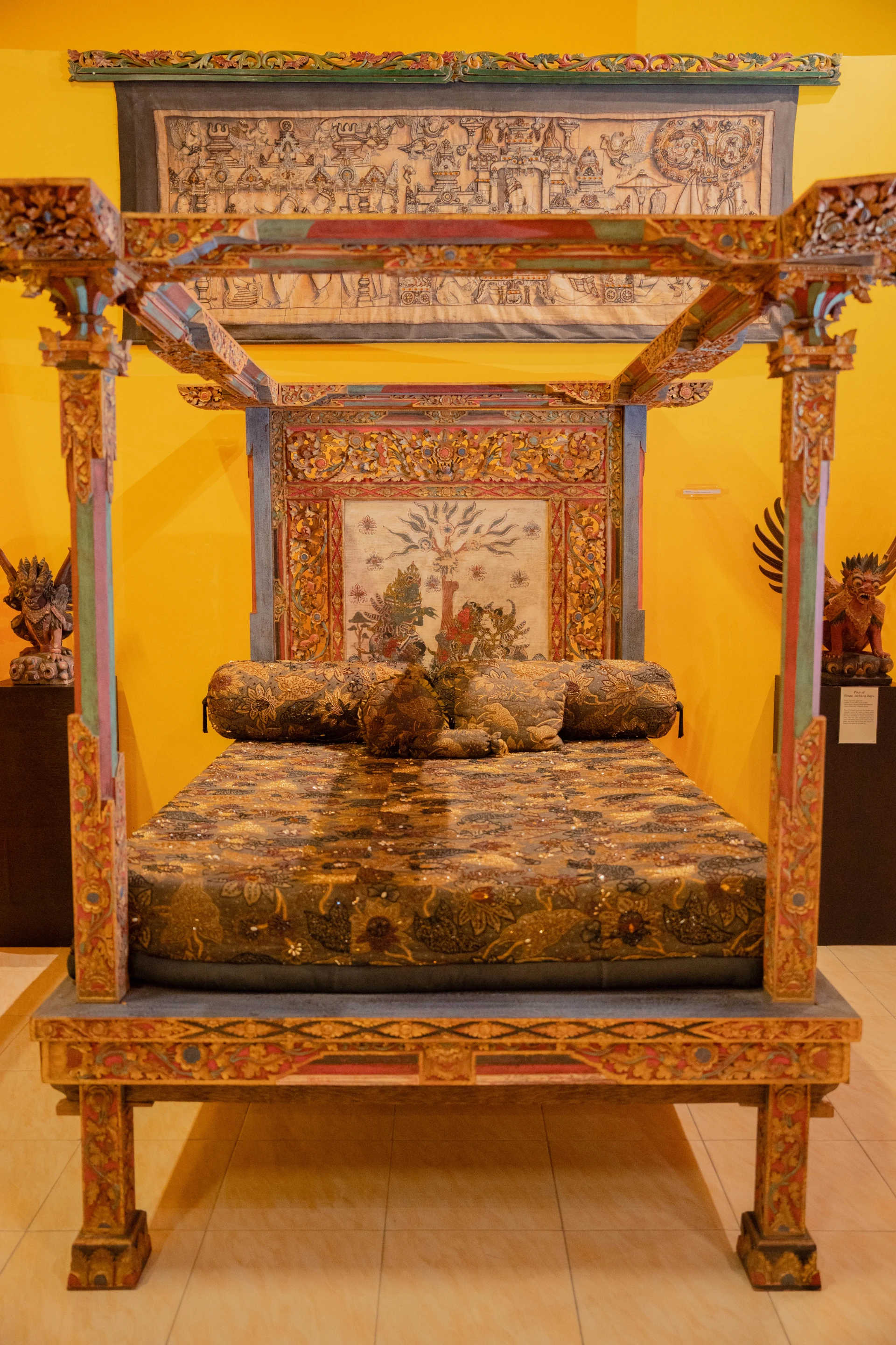 Wooden tray of ancient beads displayed against a backdrop of Balinese ornamental craftsmanship.