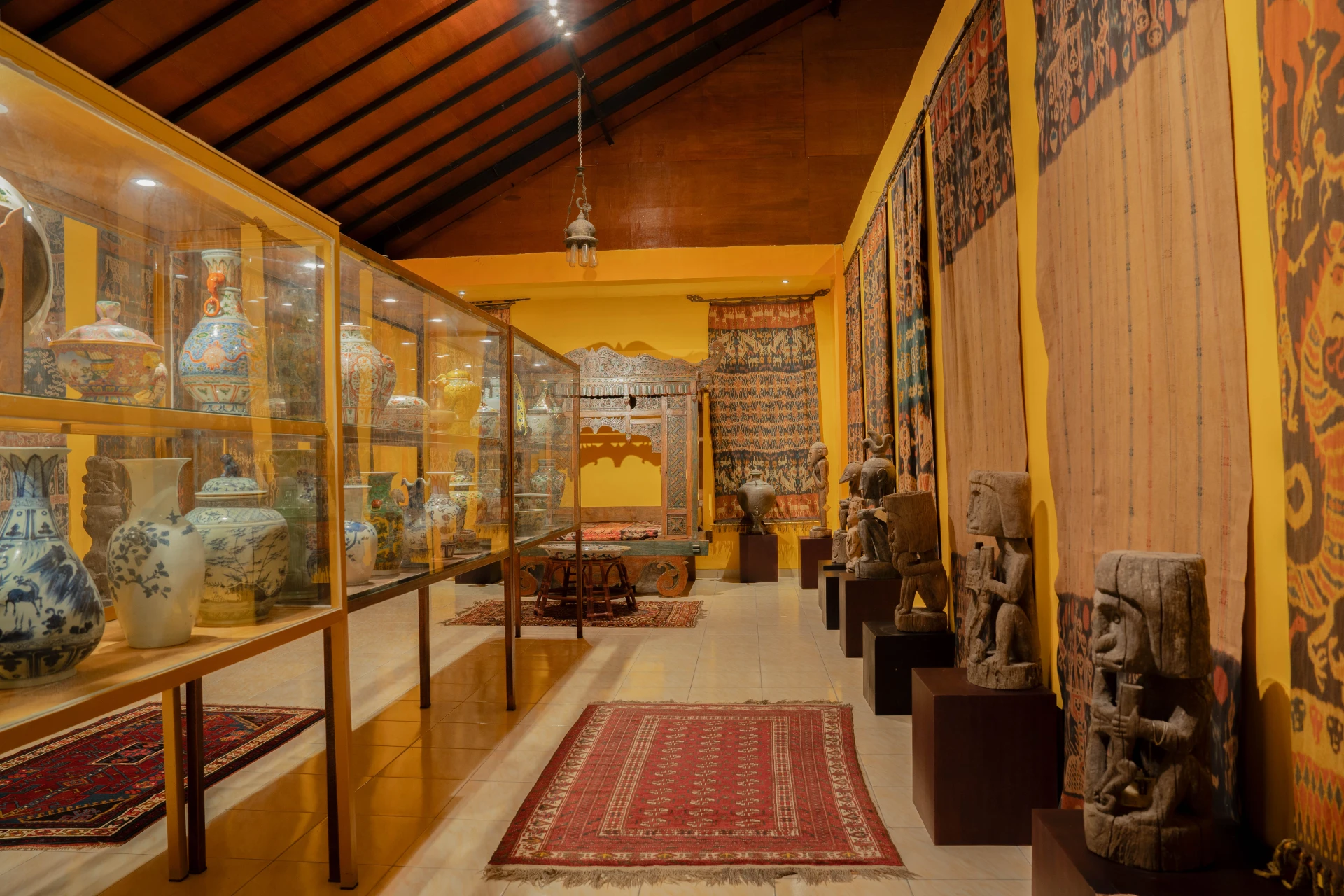 Intricate Balinese wood-carved platform draped with red traditional ikat fabrics, Museum Peter Bloch Collection.