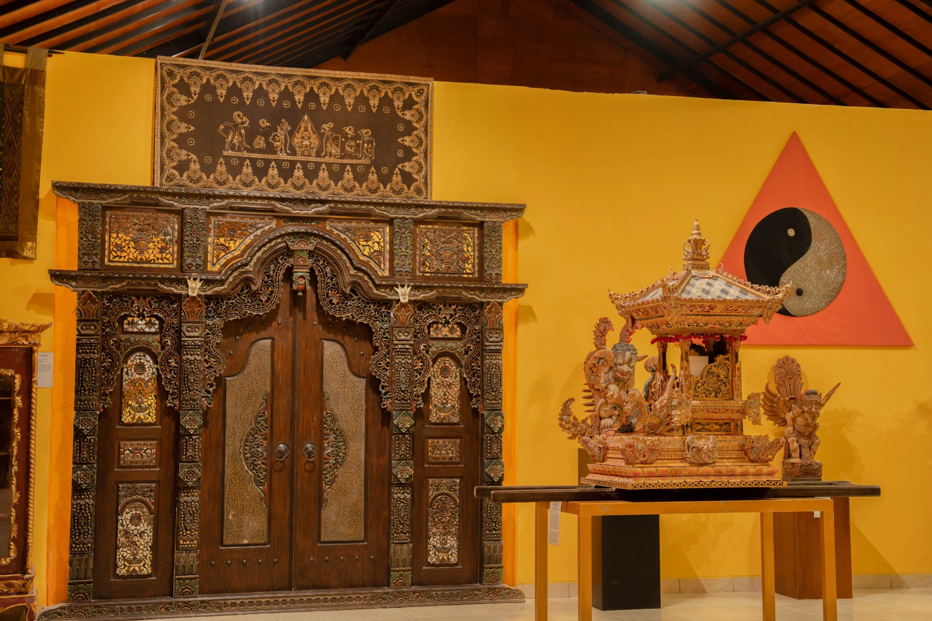 Traditional Balinese carved wooden doorway with intricate ornaments and ceremonial textiles, Annemarie Kipar Room.